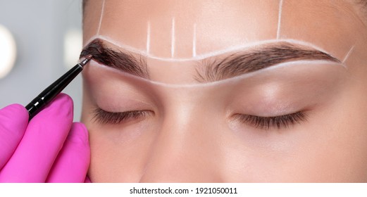 girl having permanent makeup tattoo on her eyebrows. Make-up artist makes markings with white paste for eyebrow tattooing. Professional makeup.