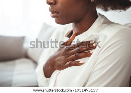 Girl having respiration problems touching chest sitting on a couch in the living room.  Woman feeling pain ache touching chest having heart attack, sad worried lady suffers from heartache at home.