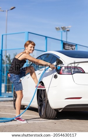 Girl having trouble removing a charging cable from her electric car.