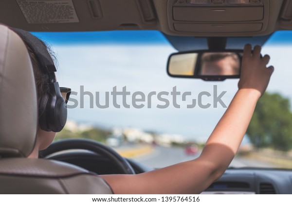 The girl in the headphones is driving on the\
highway in California. View from the back seat of the car on the\
windshield, road and the\
driver