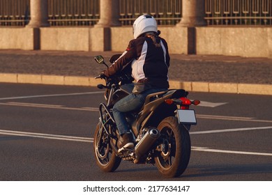 A Girl In A Helmet Rides A Motorcycle In The Evening City. Young Woman Motorcyclist Travels On A Motorbike.