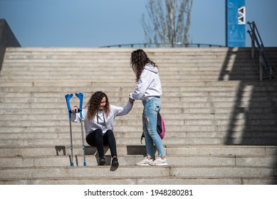 A Girl Helping Her Friend With Crutches To Get Up