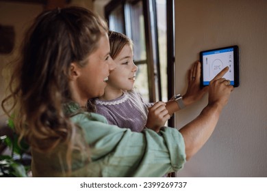 Girl helping mother to adjust, lower heating temperature on thermostat. Concept of sustainable, efficient, and smart technology in home heating and thermostats. - Powered by Shutterstock