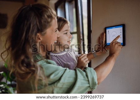 Girl helping mother to adjust, lower heating temperature on thermostat. Concept of sustainable, efficient, and smart technology in home heating and thermostats.