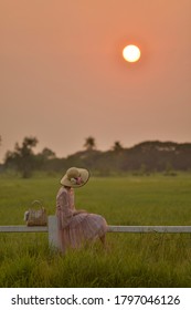 A girl and her beautiful bamboo hat is sitting wooden fence in grass field in sunset time