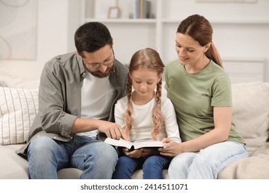 Girl and her godparents reading Bible together on sofa at home - Powered by Shutterstock