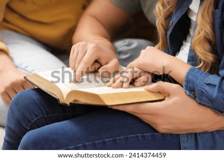 Girl and her godparents reading Bible together indoors, closeup
