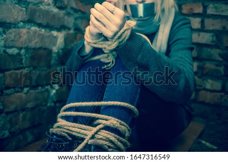 girl with her hands and feet tied and her mouth taped up is sitting in the basement. Concept of kidnapping, violence