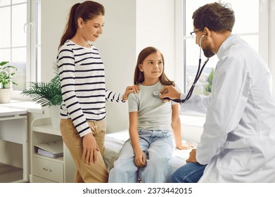 Girl with her mother in clinic for medical checkup. Male family doctor with stethoscope examining child's lungs, breathing and heartbeat at the hospital. Pediatrician checking patient in exam room. - Powered by Shutterstock