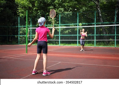 Girl with her mother play tennis on the tennis court, view from the back