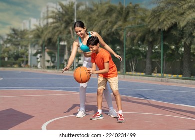 Girl and her younger brother, teenager, play basketball on modern basketball court under open sky. - Powered by Shutterstock