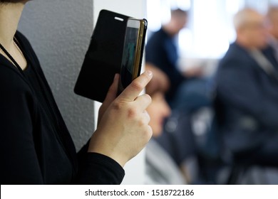 The Girl Hid Around The Corner And Shoots What Is Happening In The Audience On A Smartphone. Hidden Shooting. Curiosity And Eavesdropping. Scenes From Life. Close-up. Shallow Depth Of Field.