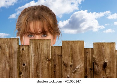 girl hiding behind a wooden fence against a blue cloudy sky.