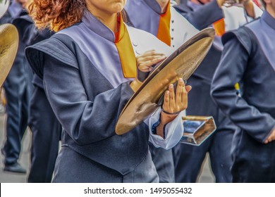 Girl in high school marching band playing the cymbals with determined looking chin - unrecognizable band members and motion blur on hands
