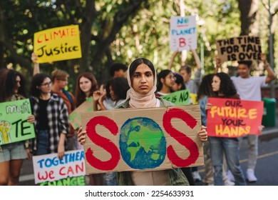 Girl in a hijab looking at the camera while holding a poster at a climate change rally. Multicultural youth activists protesting against global warming. Teenagers joining the global climate strike. - Powered by Shutterstock