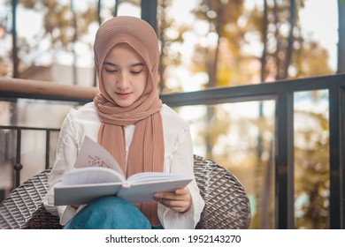 
A Girl In A Hijab Is Reading Casually On A Chair