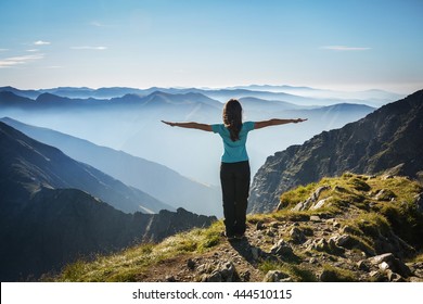 Girl hiker with arms wide open in the top of the mountain watching a beautiful scenery