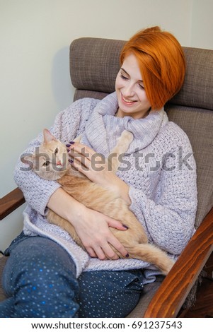 Girl hipster in home clothes hugging a pet. Red head girl in pajamas holding red fluffy cat.
