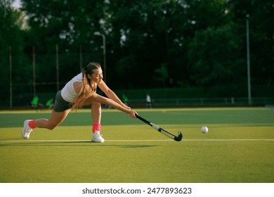 girl hockey player plays field hockey on a sunny day, female hockey player hits the ball with a stick, field hockey concept - Powered by Shutterstock