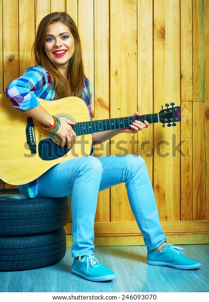 Girl hold guitar, sitting on a car  wheels\
against wooden background.