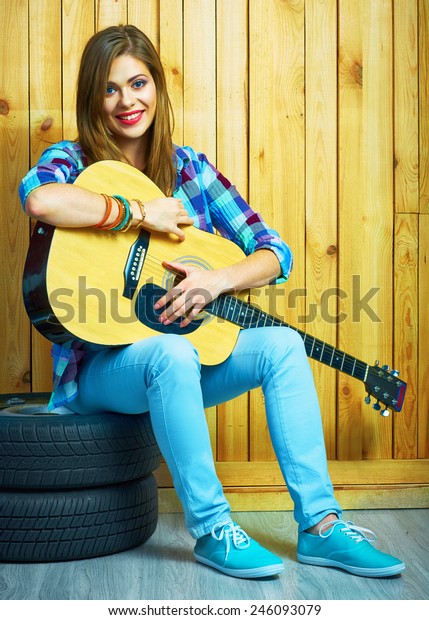 Girl hold guitar, sitting on a car  wheels\
against wooden background.