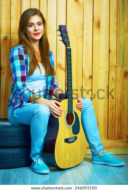 Girl hold guitar, sitting on a car  wheels
against wooden background.
