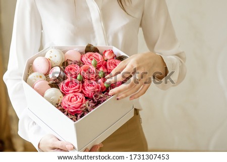 Girl hold a heart shaped box with fresh flowers pink roses and french sweets macarons in the hands.Female receive gift for mother's day,valentines,women day,birthday.Florist at work.close up.