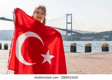 Girl hold Turkish flag near Bosphorus bridge (aka15 July Martyrs Bridge or 15 Temmuz Sehitler Koprusu) in Ortakoy, Istanbul, Turkey. Patriotism. Turkish National Sovereignty and and Children's day.
