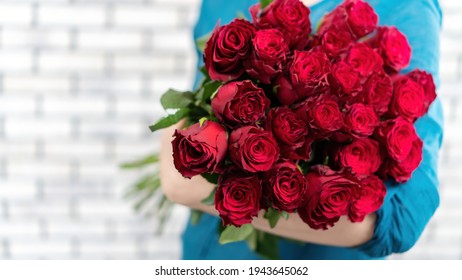 The girl is holding an armful of luxurious red roses on a white brick wall background. Greeting card with a large bouquet of red roses with copy space. Flower delivery banner. - Powered by Shutterstock