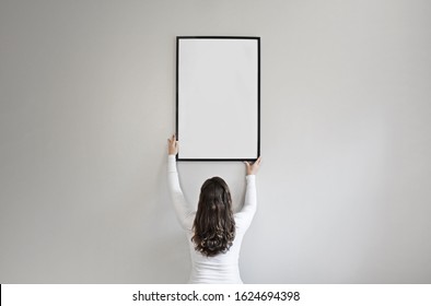 Girl holding black photo canvas frame against wall, black hair, white sweater - Powered by Shutterstock