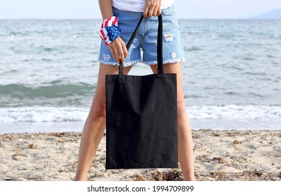 Girl Is Holding Black Tote Bag Canvas Fabric For Mockup Blank Template Isolated On Beach And Sea Background.