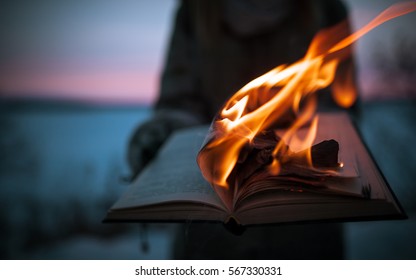 A girl holding a book burning in nature in winter at sunset