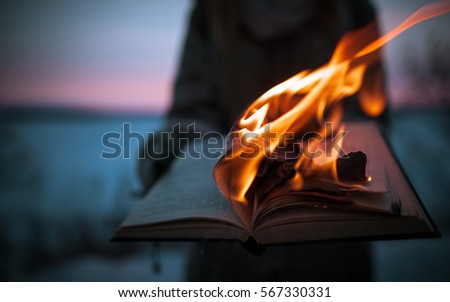 A girl holding a book burning in nature in winter at sunset