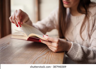 Girl holding a book wearing in warm wool pullover with red gel polish manicure. Wood retro background. Student woman concept.