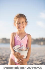 Girl Holding Bucket Of Shells On Beach