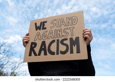 Girl holding a cardboard banner sign with slogan We Stand Against Racism. Woman with placard at Black Lives Matter protest rally demonstration. - Powered by Shutterstock