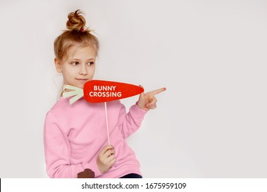The girl is holding a carrot with the inscription Bunny crossing. Cheerful portrait of a girl in pink on a light background with space for text. happy Easter. Preparing for Easter