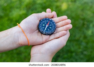 Girl holding the compass. Hands of a teenager girl holding a liquid compass. Green grass background. Copy space. Red compass needle points north. Orienteering on the ground. Selecting the direction
