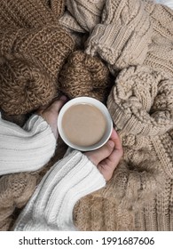 A Girl Holding A Cup Of Cappuccino On Piles Of Brown Sweaters. Aesthetic Concept