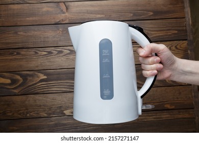 girl holding an electric kettle on a wooden background. - Shutterstock ID 2157271147