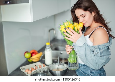 Girl holding flowers in the kitchen, home with flowers, eggs, fruits on the table.