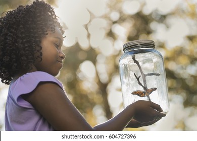 A girl holding a glass jar with a butterfly inside it,