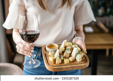 Chica sosteniendo vino tinto de cristal y plato de madera con queso. Deliciosa mezcla de queso con nueces, miel. Plato de degustación en un plato de madera. Comida por vino.