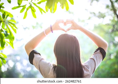 Girl Holding Hands In Heart Shape Framing Over Heads Sun At Sunlight In Garden