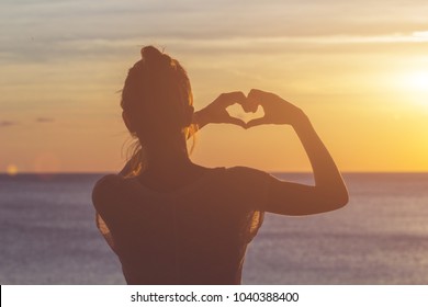 Girl holding a heart - shape symbol with her hands / fingers.