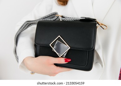 Girl Holding Her Handbag, Close-up. Small Fashionable Women's Leather Clutch Bag With Fabric Strap In Shoe Tone. Girl's Traditional Clutch Bag With Brooch. Handbag Made Of Fine Coloured Genuine Leathe