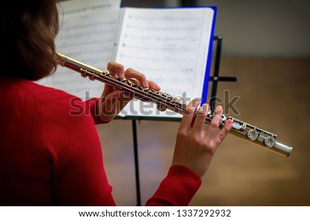 The girl is holding a large concert flute (in hands close-up). Professional musician at the rehearsal. A woman plays the transverse flute.