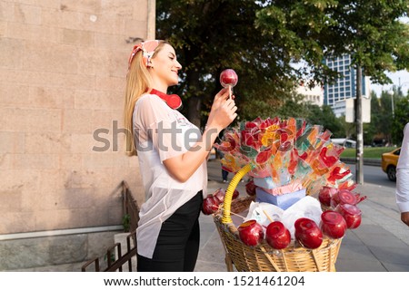 Girl holding a lollipop. Beautiful happy blond girl in the street. Young woman eating a piece of candy.