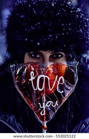 Girl holding lollipop with sign "Love you" on a snowy evening
