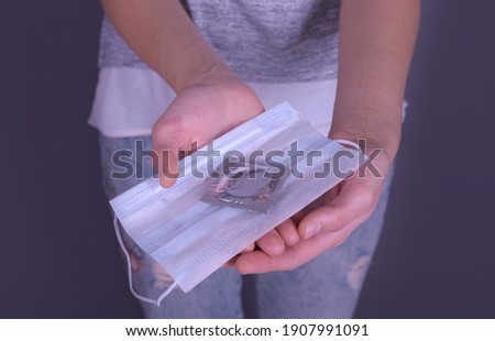 The girl is holding a medical mask and a condom in the package as two items of protection against viruses